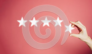 Woman`s hand put the stars to complete five stars. Customer satisfaction concept. copy space and pink background. giving a five