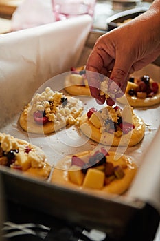 A woman`s hand puts crumble on fresh buns with fruit, ready to bake in the oven.