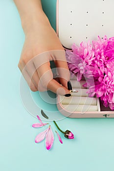 Woman`s hand puts diamond ring in the jewellery box. Beautiful accessory on blue with pink flowers