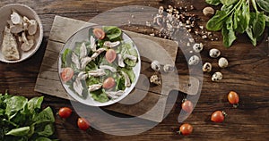 A woman`s hand puts half of red tomatoes on plate with shpinach and meat. Top view of background with quail eggs