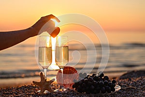 A woman`s hand puts a heart on glasses of champagne on the beach against the backdrop of sunset. Preparing for a romantic evening.