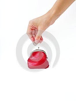 A woman`s hand puts money in a red purse with a metal lock on a white background. Saving money.