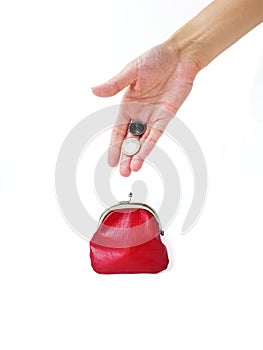 A woman`s hand puts money in a red purse with a metal lock on a white background. Saving money.