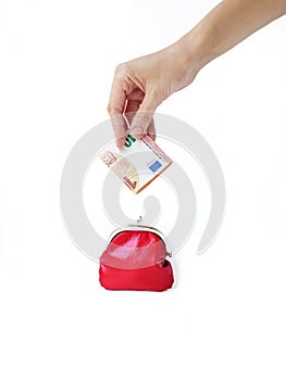 A woman`s hand puts money in a red purse with a metal lock on a white background. Saving money.