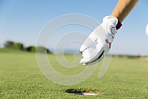 WomanÃÂ´s hand putting a golf ball into hole.