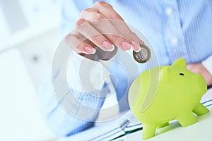 Woman`s hand putting money coin in green piggy bank close-up. Growing business, pension and insurance savings concept.