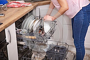 Woman`s hand putting a white plate into the dishwasher a household chore