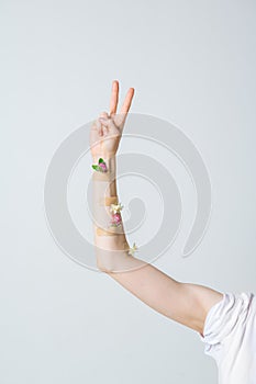 Woman`s hand raised up in peace gesture decorated by flowers. Concept photo for ecological, beauty or feminist blog