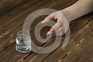 A woman`s hand reaches for a wine-glass with alcohol, a wooden background, a close-up, a ghastly alcoholism