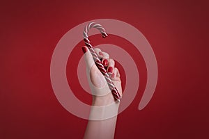 Woman`s hand with red manicure nails holding christmas candy cane on red background