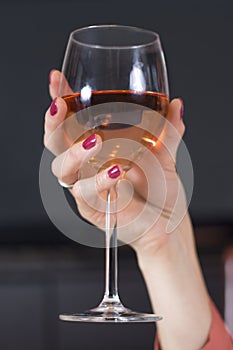 Woman`s hand with red nails and a wedding ring on her finger holds a glass of wine.