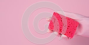 A woman's hand in a rubber glove holds a cleaning sponge on a pink background. Close-up. Copy space