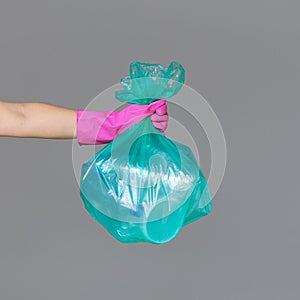 A woman`s hand in a rubber glove holds a transparent green garbage bag with empty plastic bottles.