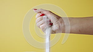 Woman's hand scoops up and sprinkles white sand on yellow studio background. Sandy particles wake up through your