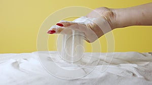 A woman's hand scoops up white loose sand on yellow studio background. Sandy particles wake up through your fingers