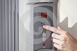 A woman's hand setting the room temperature on a digital programmable oil heater