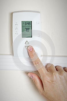 A woman's hand setting the room temperature on a modern digital programmable thermostat