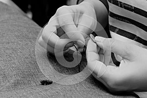 Woman`s hand sews with a needle in atelier, gray fabric, horizontal, black and white photo. Small business concept
