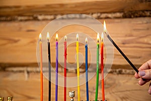 A woman's hand with a shamash candle lights the Hanukkah candles at the table