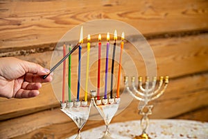 A woman& x27;s hand with a shamash candle lights the Hanukkah candles at the table
