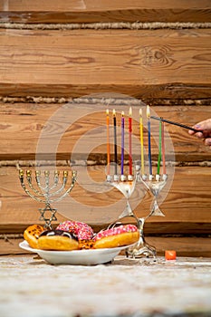 A woman's hand with a shamash candle lights the Hanukkah candles at the table with donuts