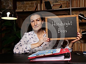 Woman`s hand showing chalkboard with phrase Hindsight Bias - closeup shot on grey background