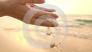 Woman`s hand with soft sand falling on tropical beach.