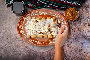 Woman's hand spooning salsa on a plate of golden potato tacos.