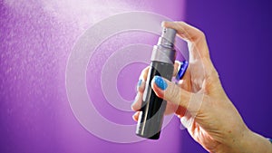 Woman`s hand with spray bottle is spraying something on purple background.