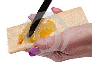 Woman's hand spreading orange marmalade on a toast