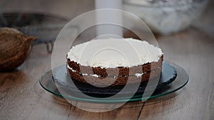 Woman`s hand spreading whipped white cream on chocolate sponge cake.