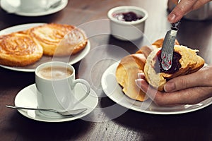 Woman's Hand Spreads Preserves on a Croissant Roll in a Cafe