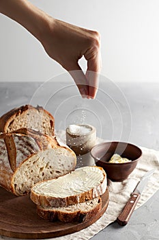 Woman`s hand sprinkling sugar artisan sliced toast bread with butter on wooden cutting board. Simple breakfast