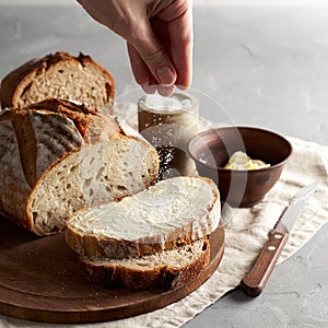 Woman`s hand sprinkling sugar artisan sliced toast bread with butter on wooden cutting board. Simple breakfast