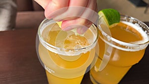 a woman's hand squeezes lemon juice into a glass of beer on the table, two glasses with a light drink