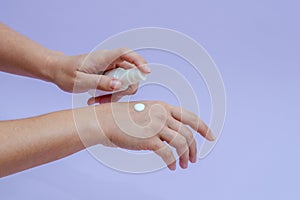 Woman's hand squeezing out cream in white tube isolated on lilac background. Beauty concept. Tube for cosmetic products