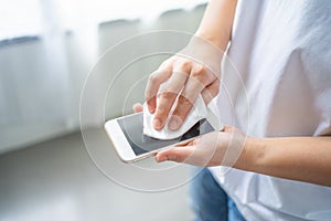 Woman`s hand standing wipe smartphone screen with disinfectant cloth at home. Close-up woman cleans her mobile phone.Woman`s han