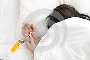 Woman& x27;s hand sticks out from under blanket, pills lie on her hand.