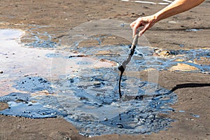 A woman`s hand stirring liquid asphalt with a wooden stick at Pitch Lake, La Brea, Trinidad island, Trinidad and Tobago photo