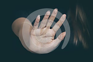 A woman`s hand with a stop gesture on a dark background. Copy space, selective focus