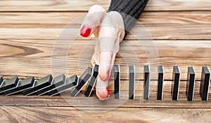 Woman`s hand stopping domino effect on the desk.