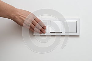 A woman's hand switches an electric switch located on a white wall