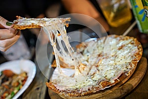 Woman`s hand take pizza pices out from pizza plate in foodtruck event, Cheese`s pizza is stretced by her photo