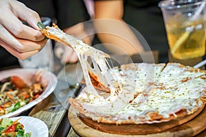 Woman`s hand take pizza pices out from pizza plate in foodtruck event, Cheese`s pizza is stretced by her photo
