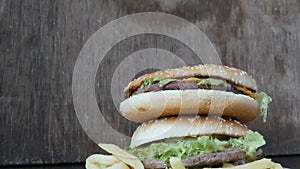 A woman`s hand takes a burger from a large mountain of three delicious juicy burgers with lettuce leaves and cheese