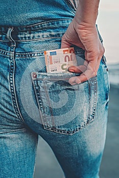 A woman`s hand takes out euro bills from the back pocket of her jeans. The concept of finance, savings, financial expenses. Close