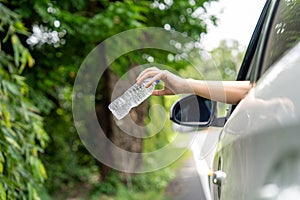 Woman's hand throwing away plastic bottle from car window on the road in green nature