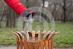 A woman`s hand is throwing away plastic bottle in a recycling bin. Hand throwing empty plastic water bottle in recycling bin