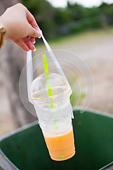 A woman`s hand is throwing the empty glass to a green bin