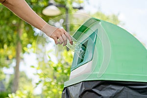 A woman's hand throws a plastic water bottle into a green trash can. Environmental conservation